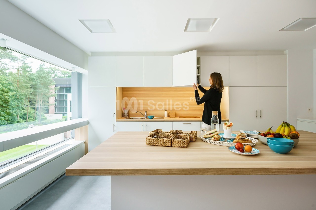 Une femme ouvre un placard dans une cuisine moderne lumineuse avec un plan de travail en bois et des aliments disposés.