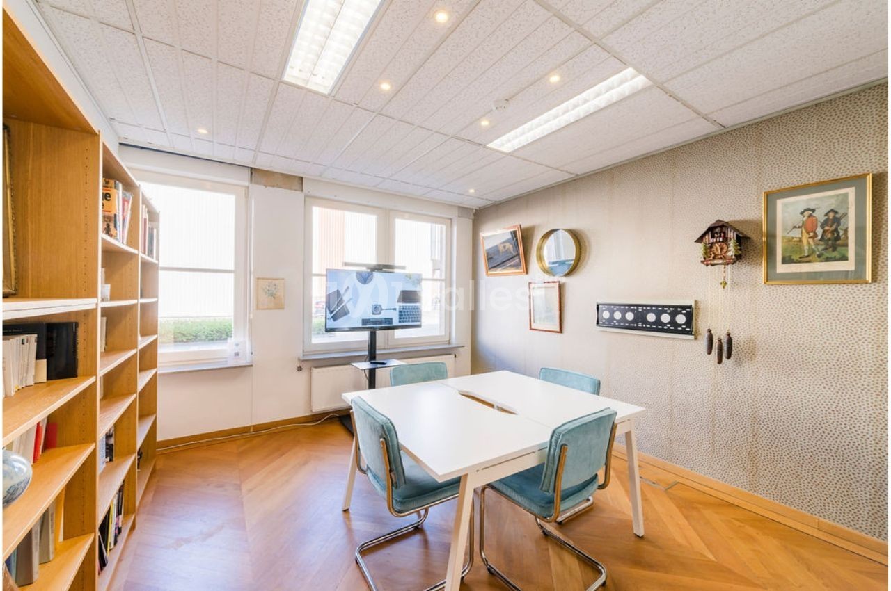 Salle de réunion lumineuse avec table blanche, chaises bleues, étagères remplies de livres et décorations murales.