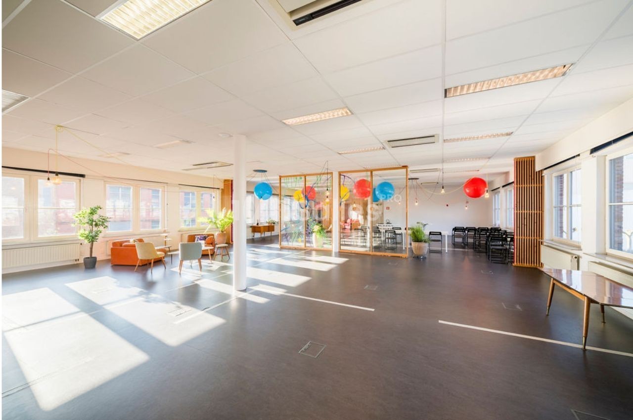 Espace lumineux avec de grandes fenêtres, mobilier moderne, ballons colorés et cloison vitrée au fond.