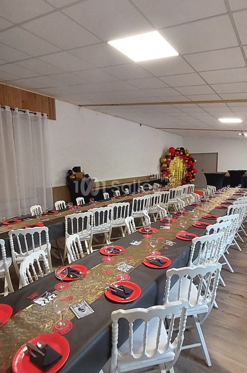 Salle décorée pour un événement avec longues tables dressées, nappes noires, assiettes rouges et décoration dorée en fond.