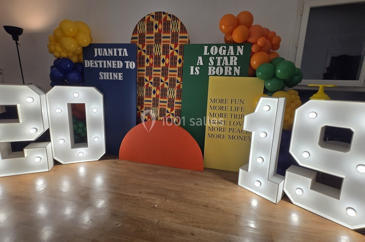 Décor festif avec ballons colorés, panneaux personnalisés et chiffres lumineux ’2019’ sur un sol en bois.