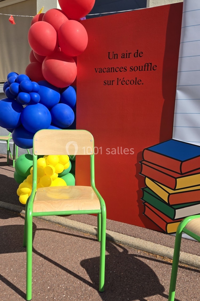 Chaise d'école devant une décoration colorée avec des ballons et un panneau mentionnant ’Un air de vacances souffle sur l…