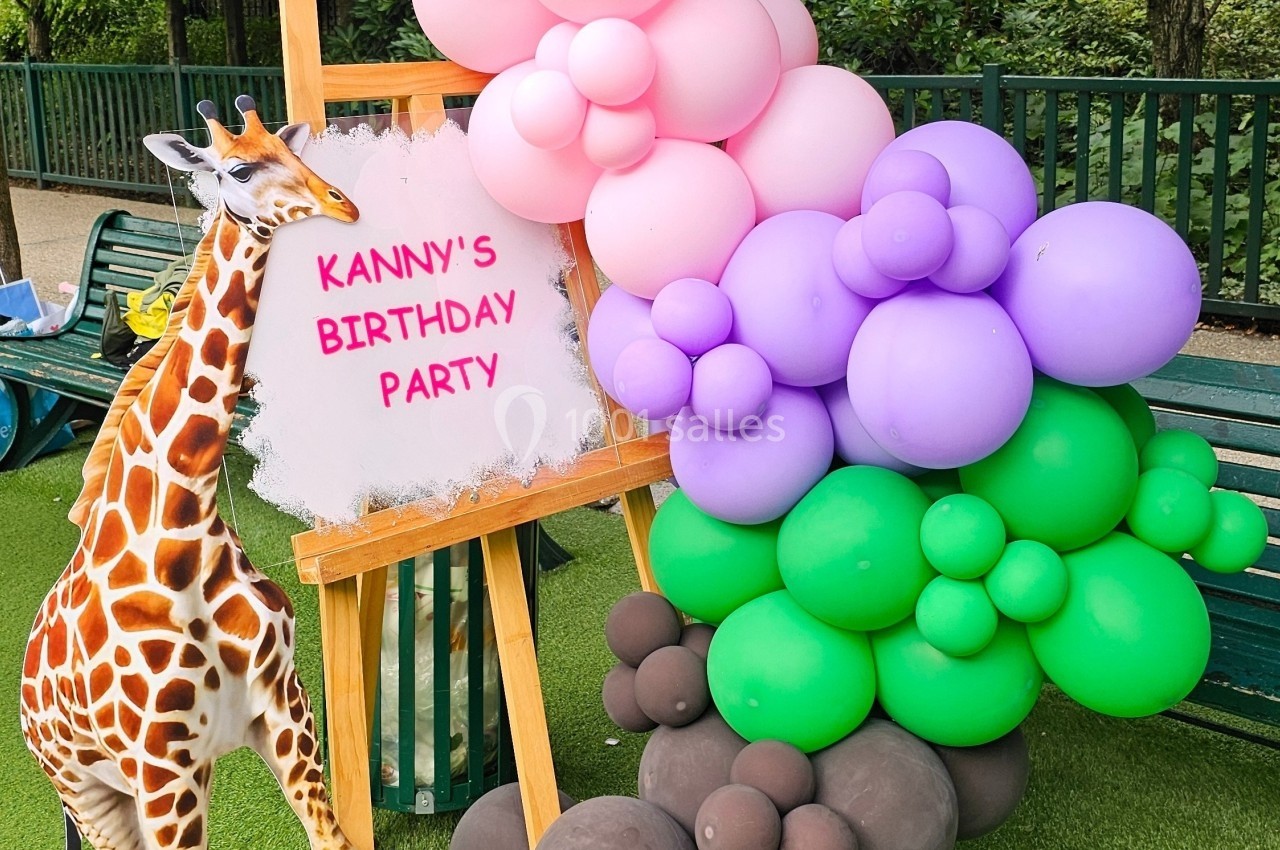 Panneau décoratif avec une girafe en carton et des ballons colorés, installé dans un espace extérieur.