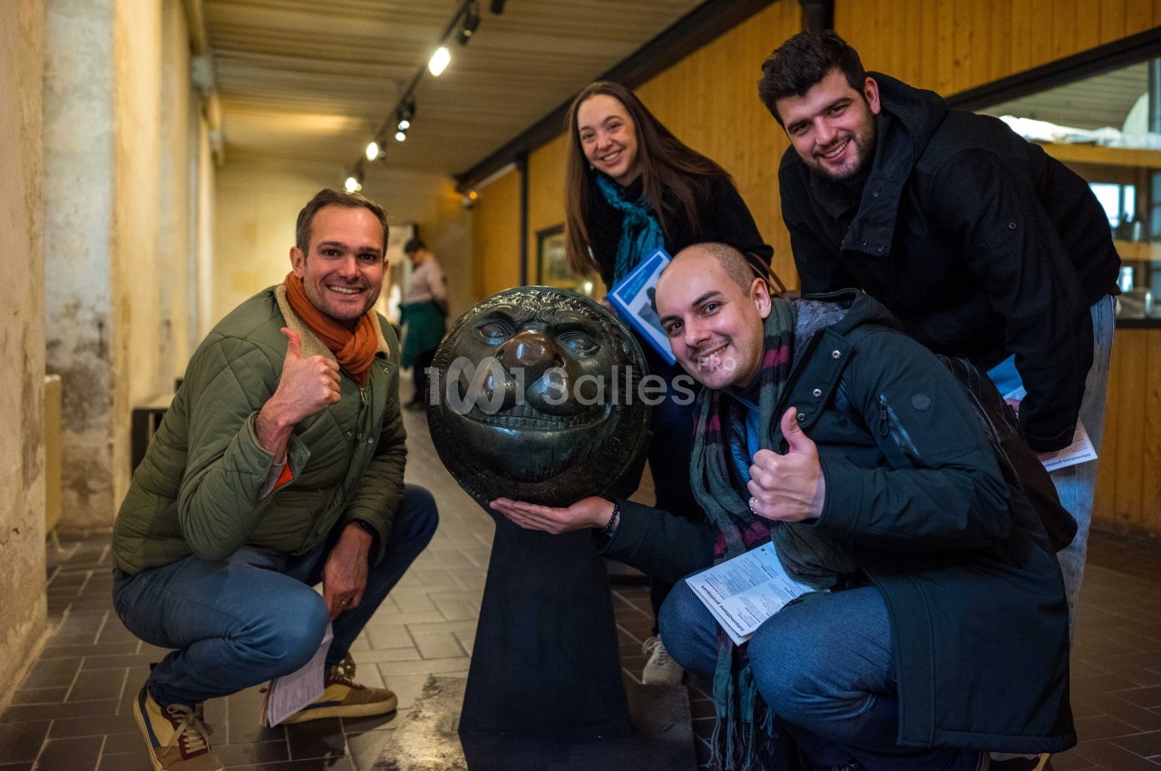 Quatre personnes souriantes posent autour d'une sculpture en forme de tête animale dans un espace intérieur éclairé.