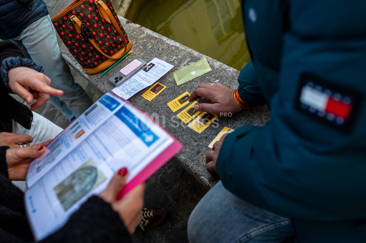 Des personnes consultent des documents et des cartes sur une table en pierre près d'un sac et d'un bassin d'eau.