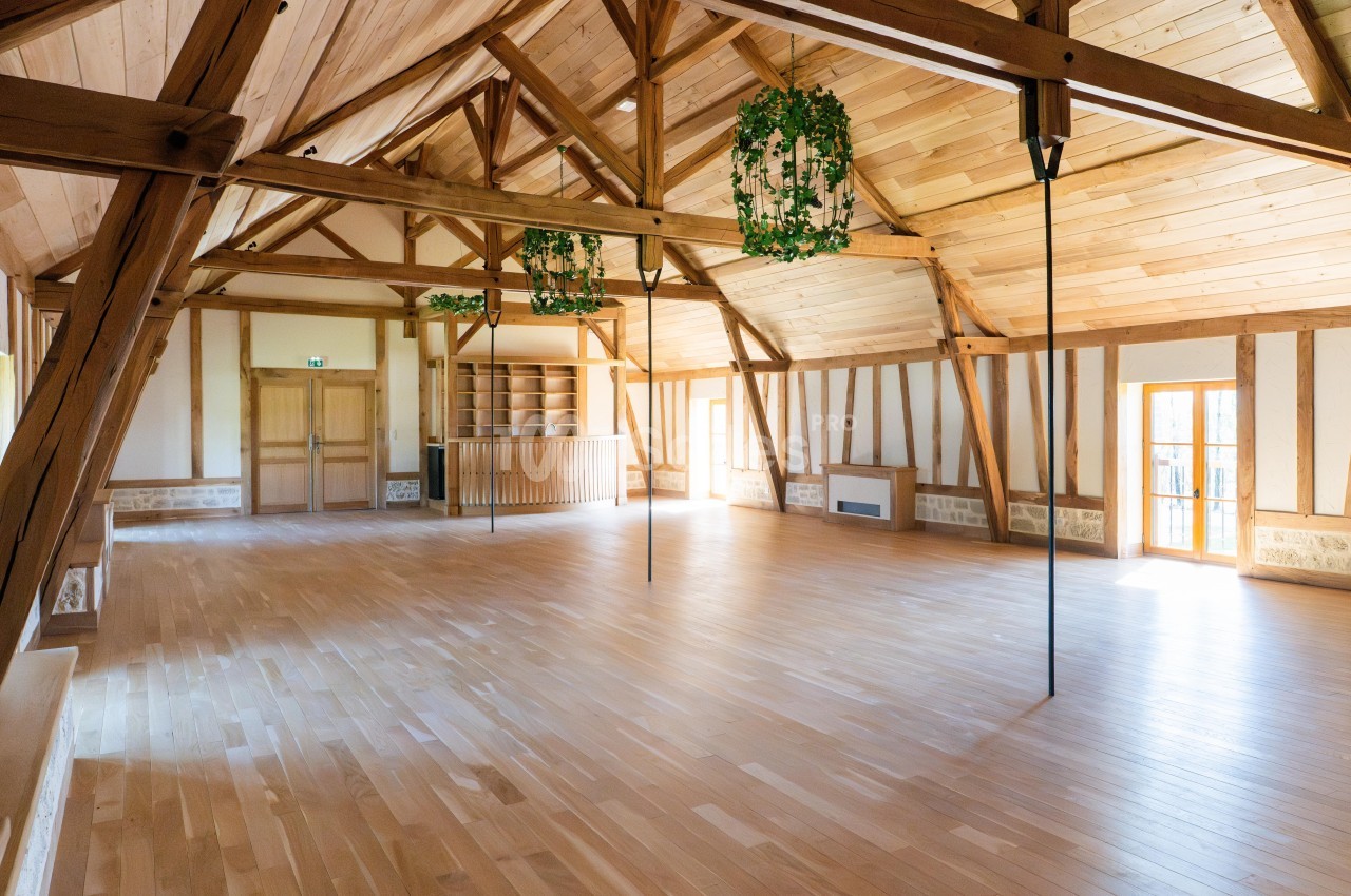 Grande salle lumineuse avec parquet en bois clair, charpente apparente et murs en bois et pierre.