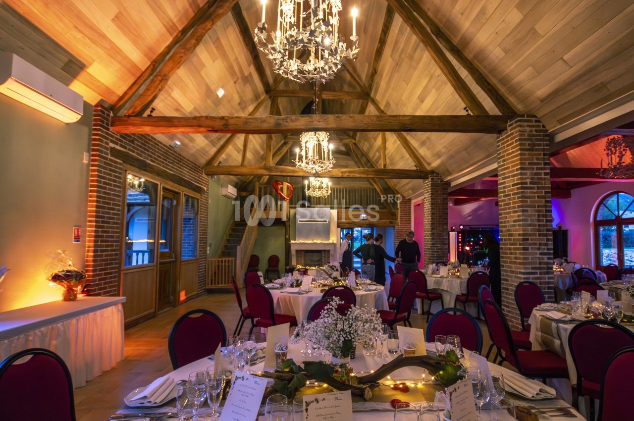 Salle de réception chaleureuse avec poutres apparentes, tables décorées et éclairage tamisé.