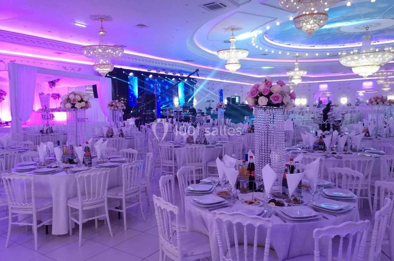 Salle de réception élégante avec tables dressées, décorations florales et éclairage coloré.