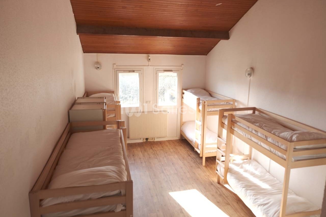 Dortoir lumineux avec lits superposés en bois, parquet au sol et plafond en bois incliné.