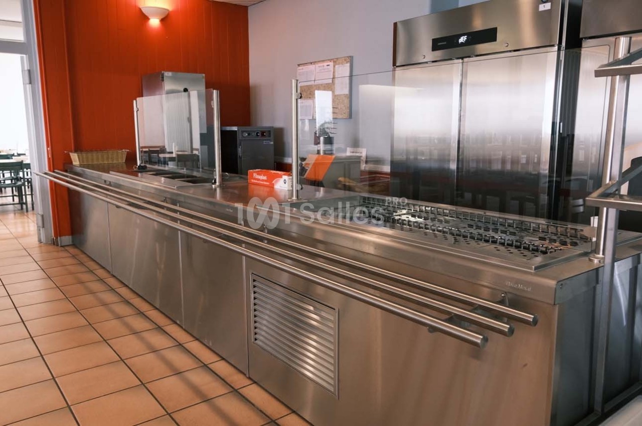 Comptoir de self-service en inox dans une cantine avec équipements de cuisine et réfrigérateurs en arrière-plan.