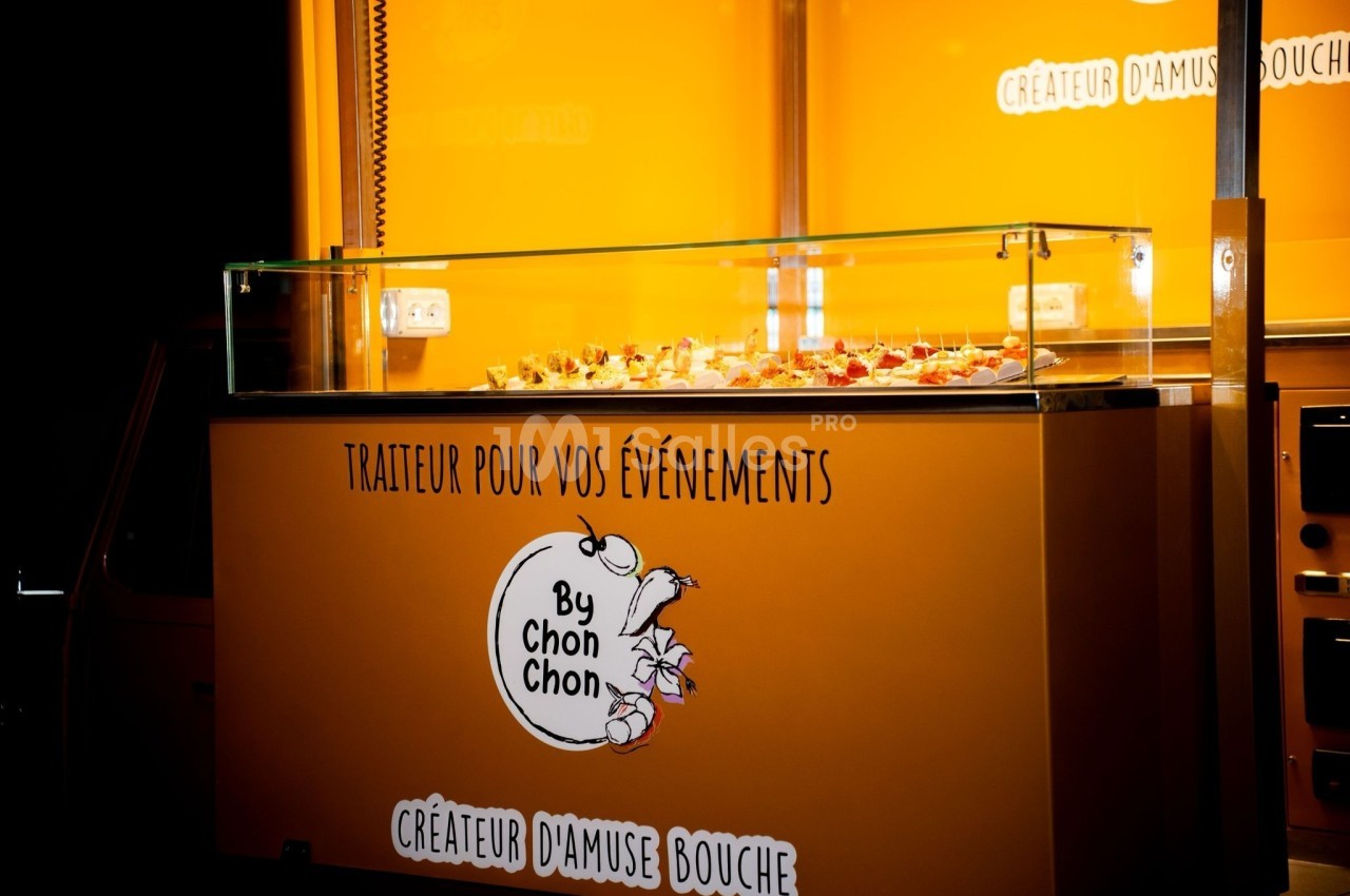 Vitrine éclairée d'un traiteur avec des amuse-bouches présentés sur un comptoir en verre, fond orange vif.