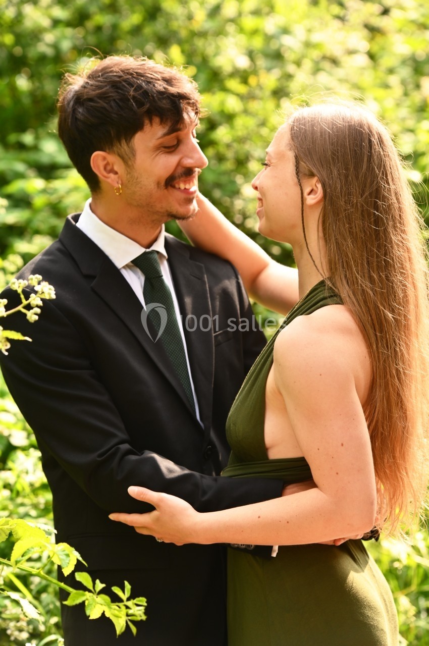 Un couple souriant s'enlace dans un jardin verdoyant baigné de lumière naturelle.