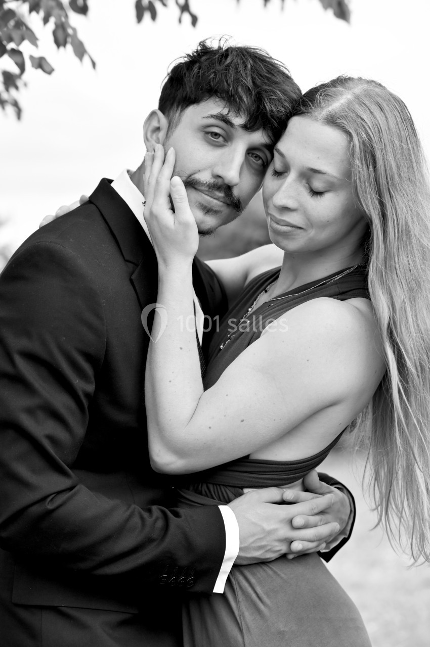 Un couple élégant en tenue formelle pose tendrement dans un cadre extérieur naturel.
