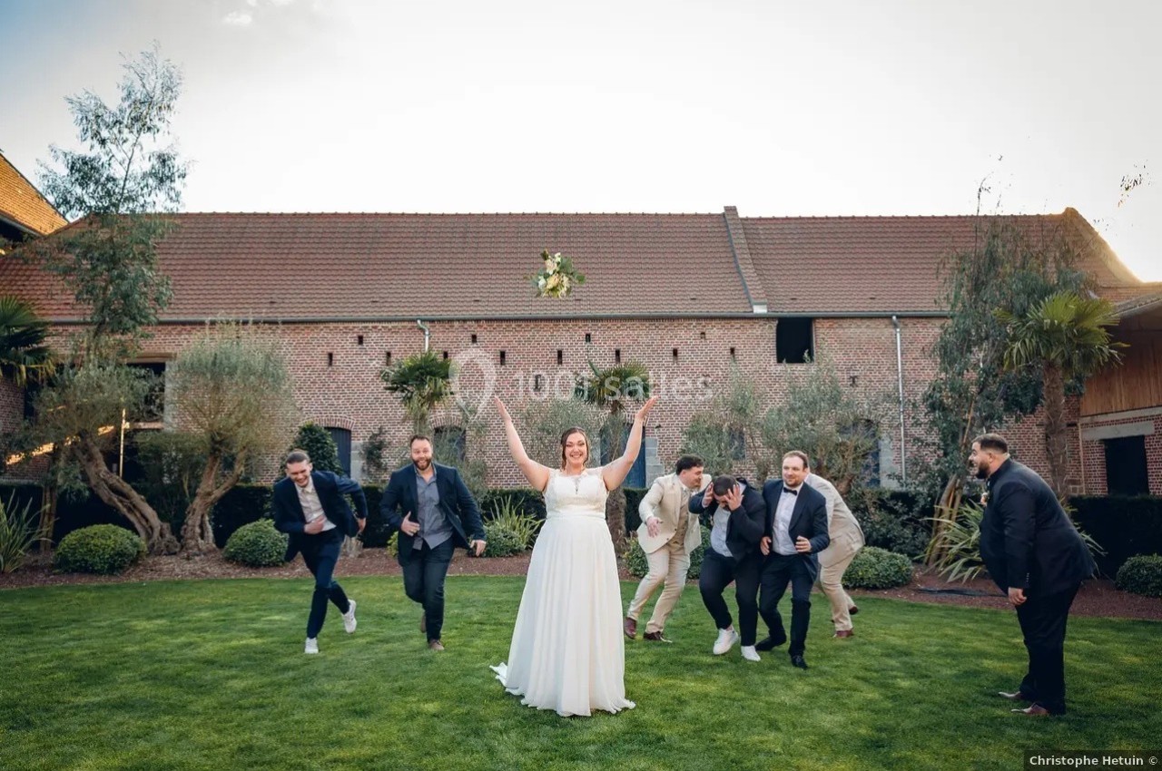 Une mariée lance son bouquet en l'air devant un groupe d'invités dans un jardin, près d'un bâtiment en briques.