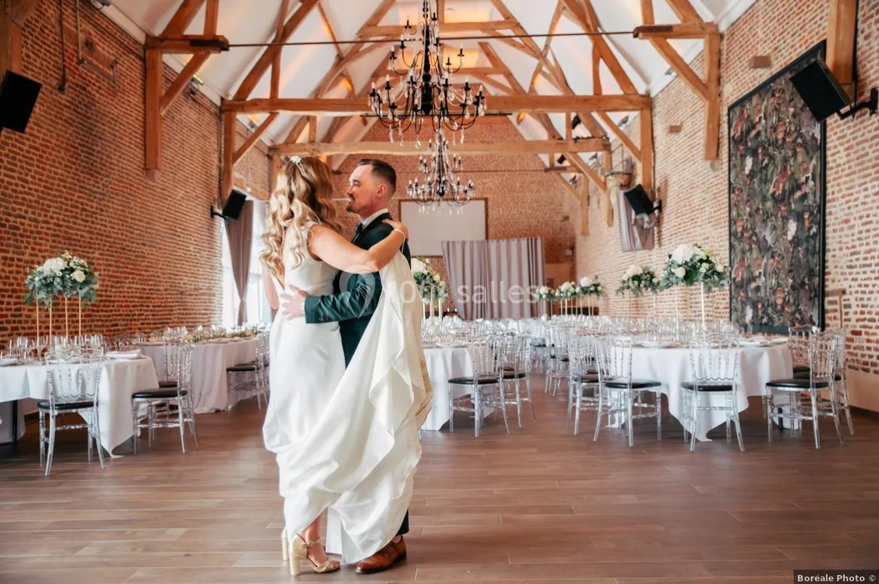 Un couple danse dans une salle de réception lumineuse avec des poutres apparentes et une décoration élégante.