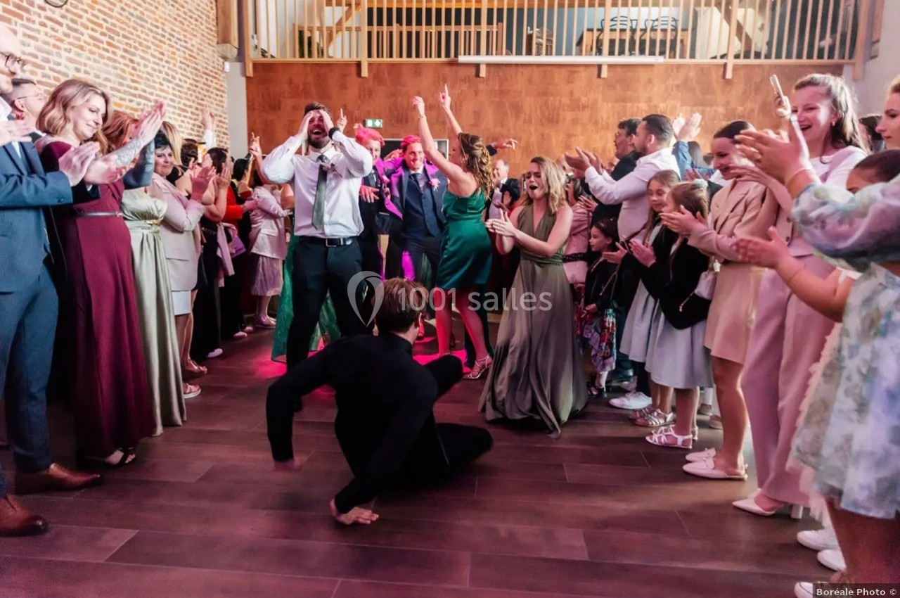 Un homme danse au centre d'une piste entouré d'invités applaudissant dans une salle de réception.