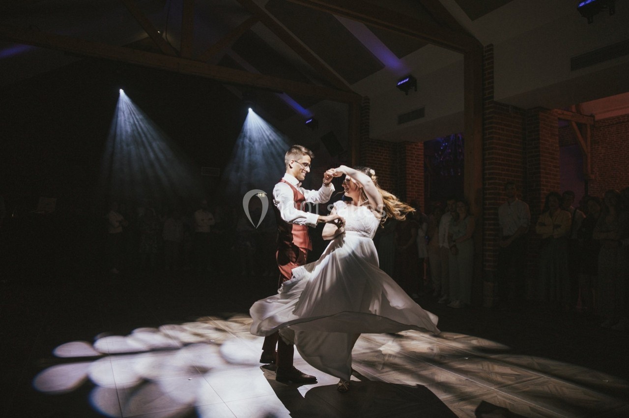 Un couple danse sous des projecteurs dans une salle sombre avec des invités en arrière-plan.
