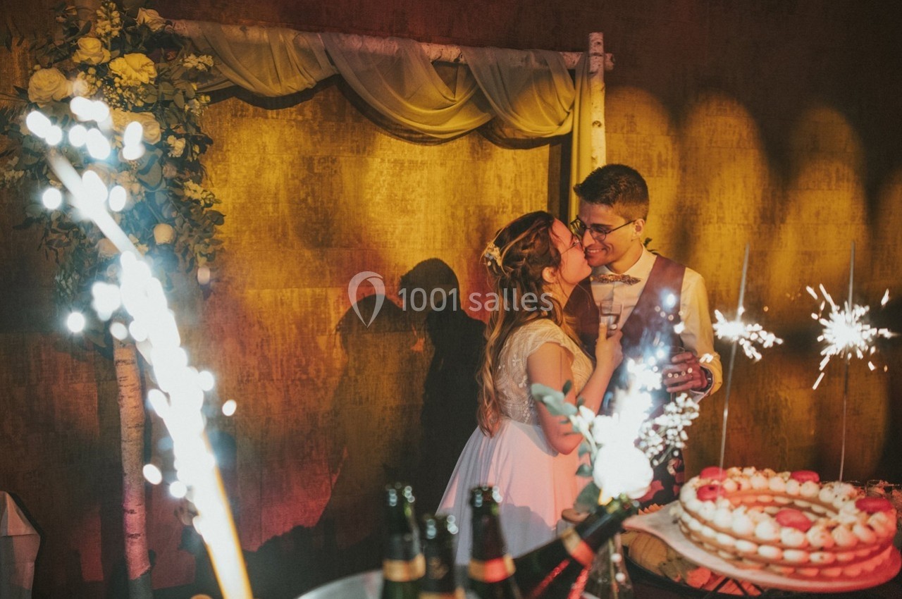 Un couple de mariés s'embrasse devant une décoration florale, entouré de lumières et de feux d'artifice.
