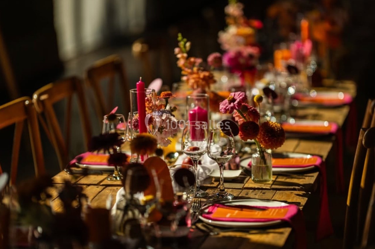 Table en bois décorée de fleurs colorées, bougies et verres, préparée pour un repas dans une ambiance chaleureuse.