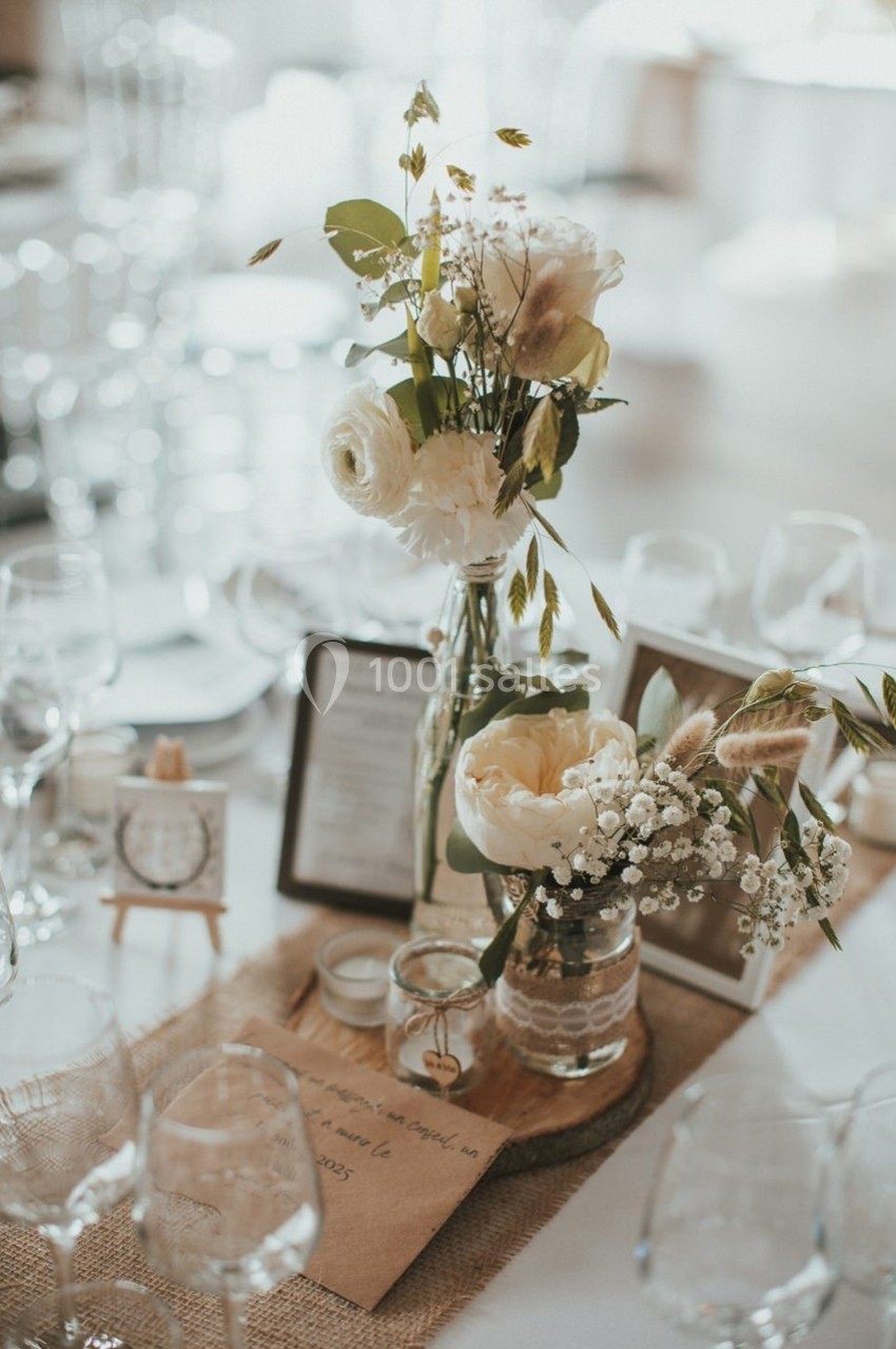 Centre de table avec fleurs blanches et feuillages dans des vases en verre, entouré de bougies et décorations rustiques.