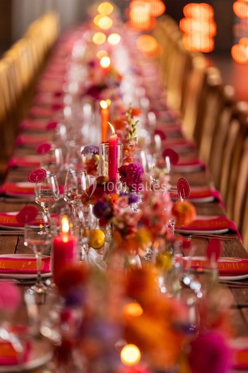 Table décorée avec des bougies allumées, des fleurs colorées et des serviettes rouges, alignée dans une ambiance chaleureuse.