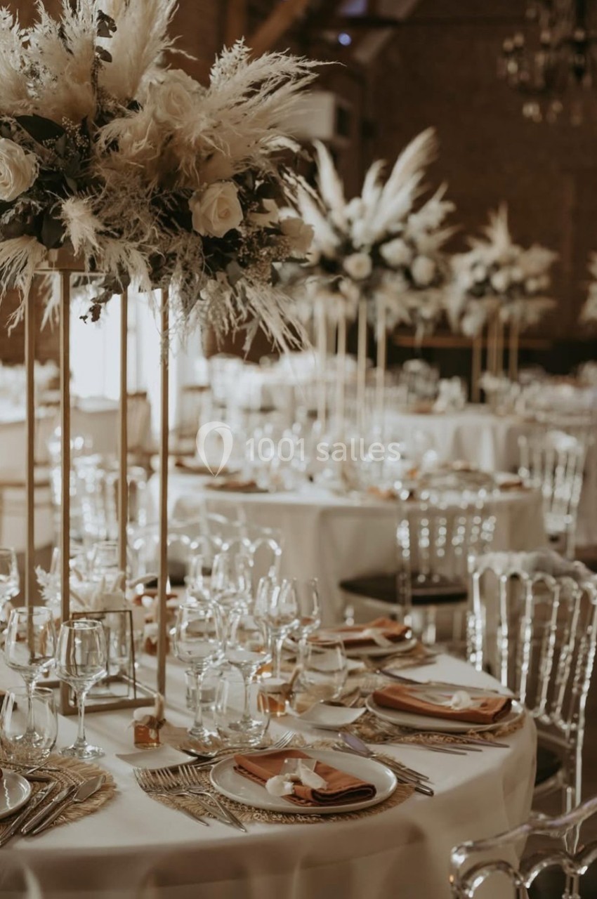 Tables de réception élégamment dressées avec des compositions florales hautes et des assiettes soigneusement disposées.