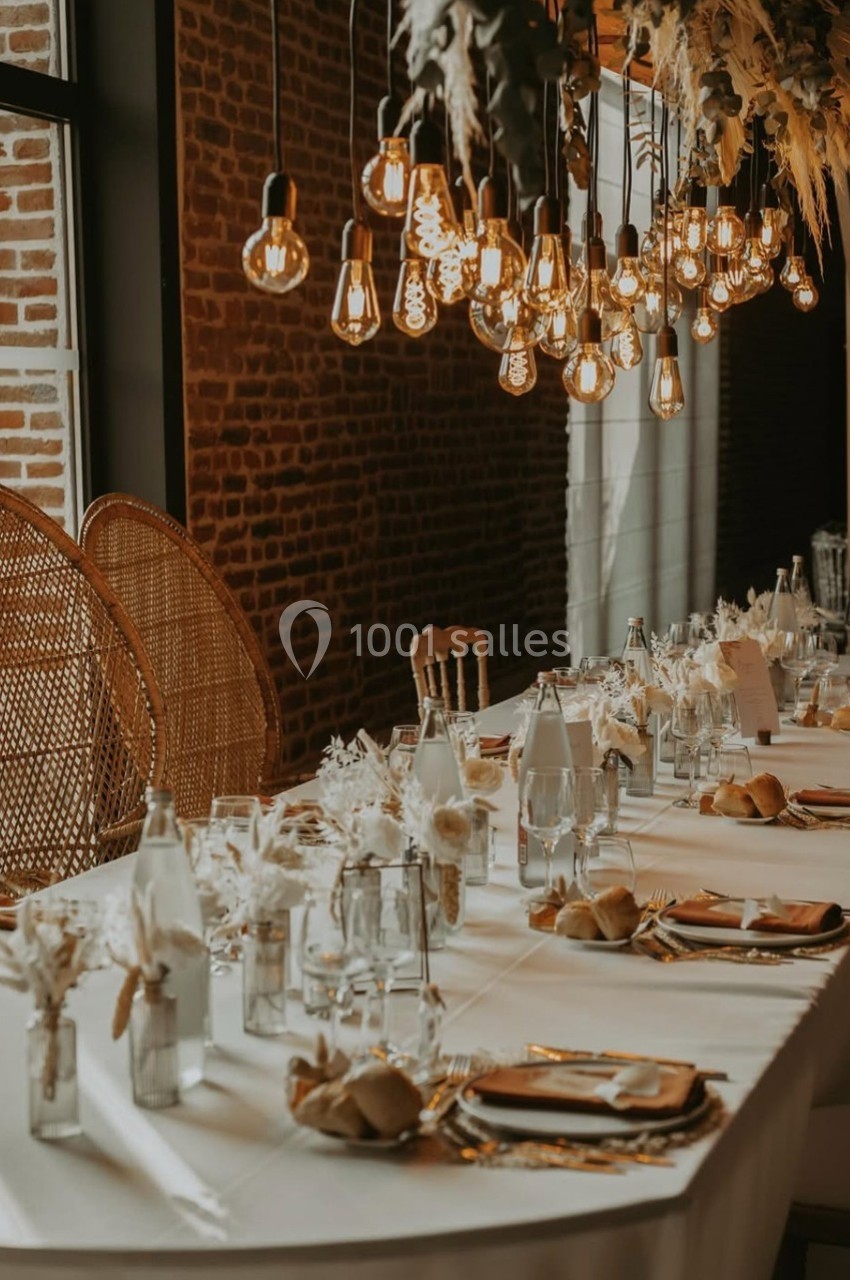 Table élégamment dressée avec vaisselle raffinée, décorations naturelles et suspensions lumineuses dans une ambiance…