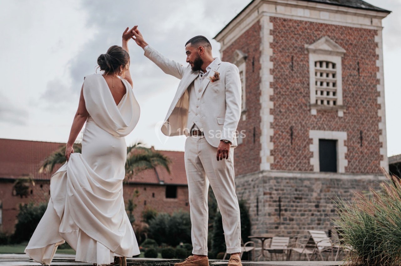 Un couple en tenue de mariage danse devant un bâtiment en briques dans un cadre extérieur.