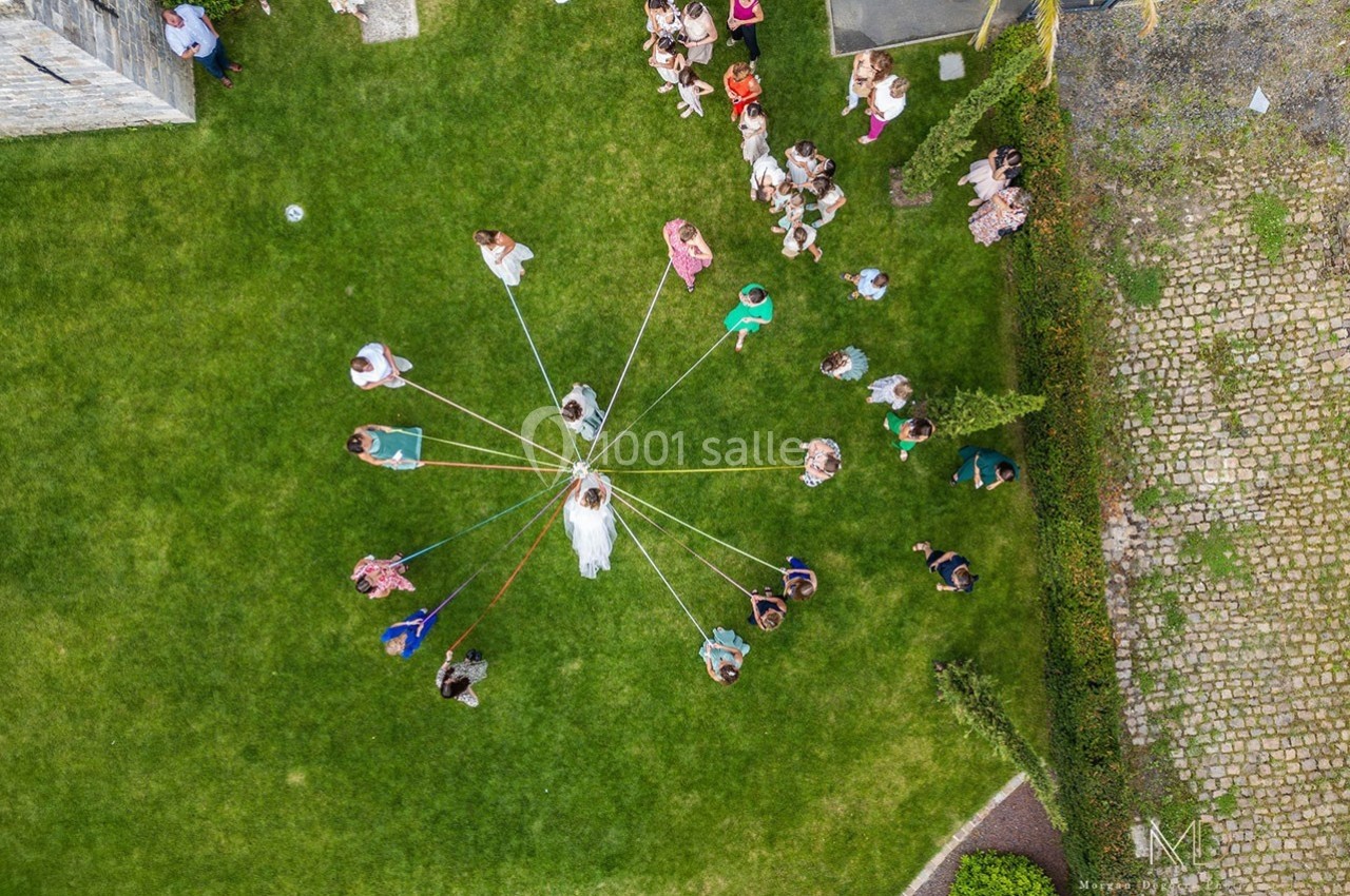 Vue aérienne d'un groupe de personnes formant un cercle autour d'une mariée tenant des rubans colorés.