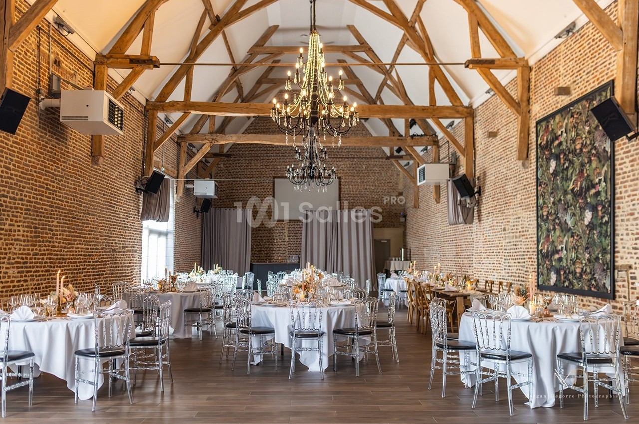 Salle de réception en briques avec charpente apparente, tables rondes dressées et lustres suspendus.