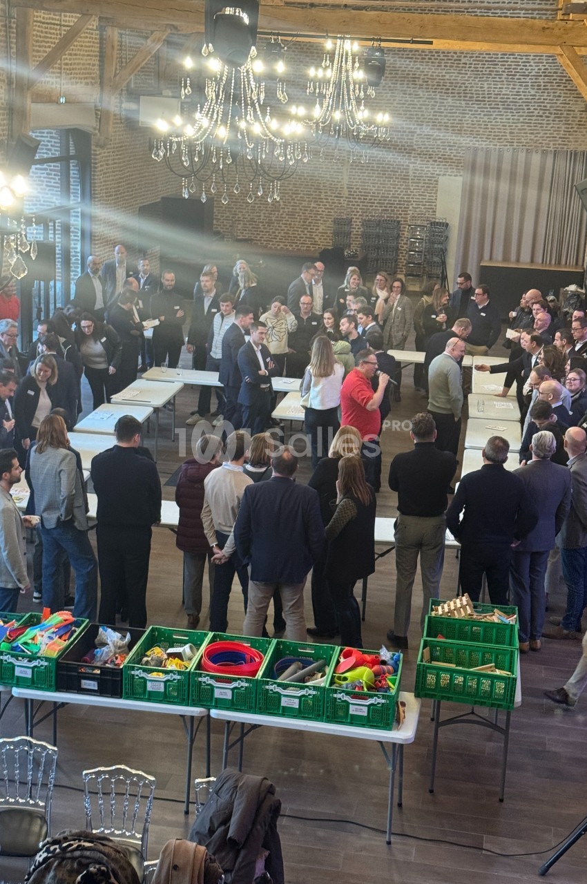 Des personnes rassemblées dans une salle avec des tables, des jouets et des caisses vertes au premier plan.