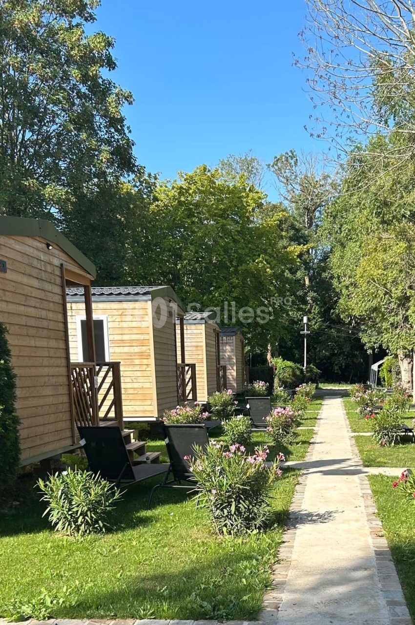 Allée bordée de mobil-homes en bois, entourée de végétation et de fleurs sous un ciel bleu.
