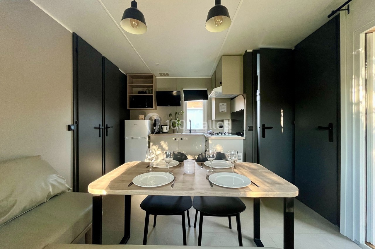 Salle à manger moderne avec table dressée pour quatre personnes, cuisine équipée en arrière-plan et éclairage suspendu.