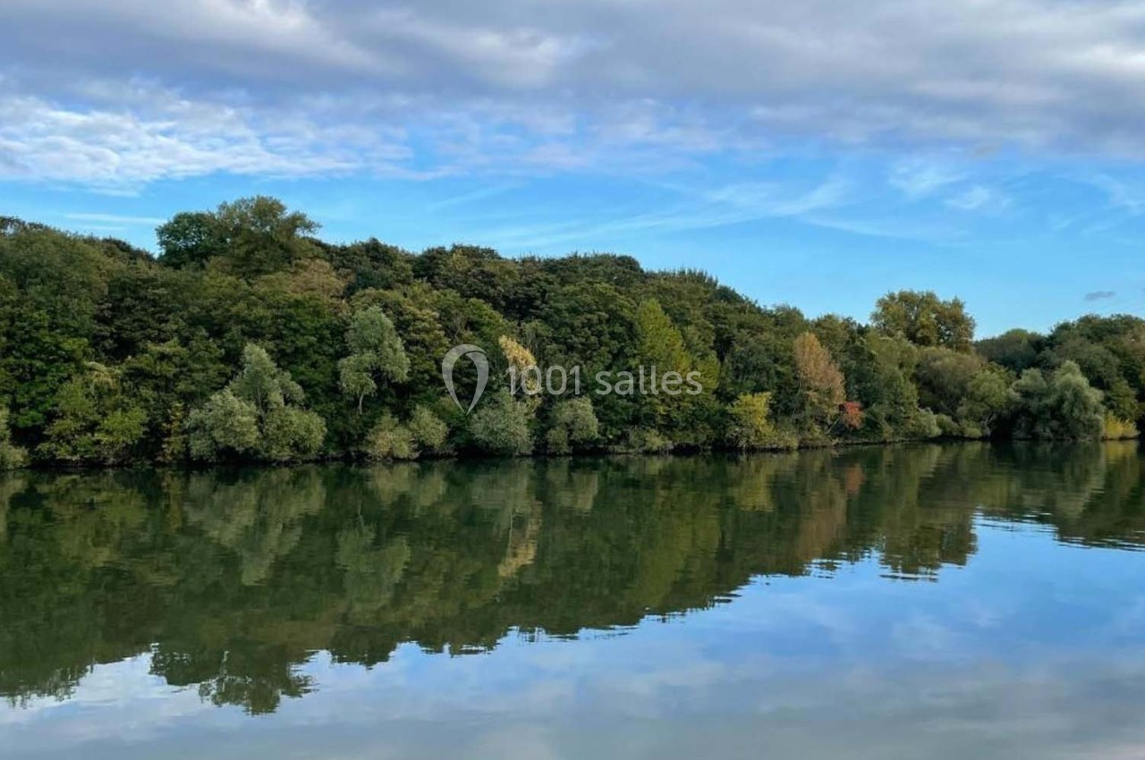 Rivière calme reflétant une forêt dense sous un ciel partiellement nuageux.