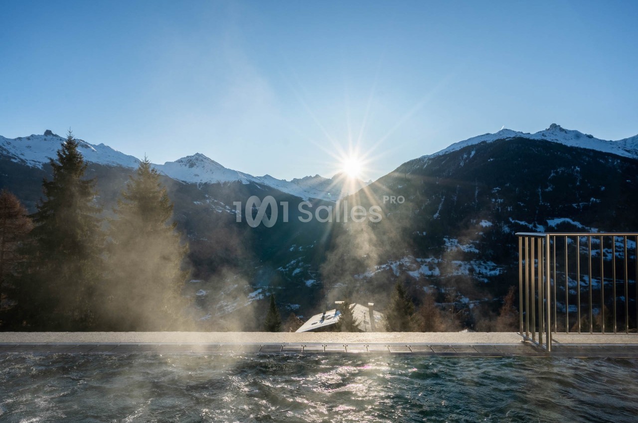 Vue sur des montagnes enneigées au lever du soleil depuis une piscine extérieure dégageant de la vapeur.
