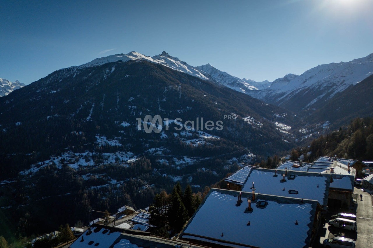 Vue aérienne d'un village de montagne enneigé entouré de sommets alpins sous un ciel dégagé.
