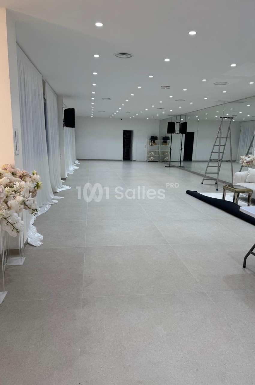 Salle lumineuse avec sol en carrelage clair, décor floral, rideaux blancs, échelle et mobilier en cours d'installation.