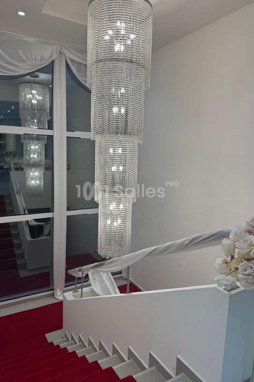 Escalier recouvert de tapis rouge avec un lustre en cristal suspendu et des décorations florales blanches.
