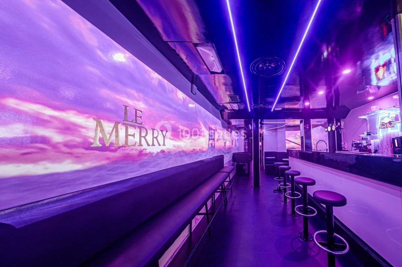 Intérieur d'un bar moderne avec éclairage violet, banquettes noires, tabourets hauts et un comptoir à droite.