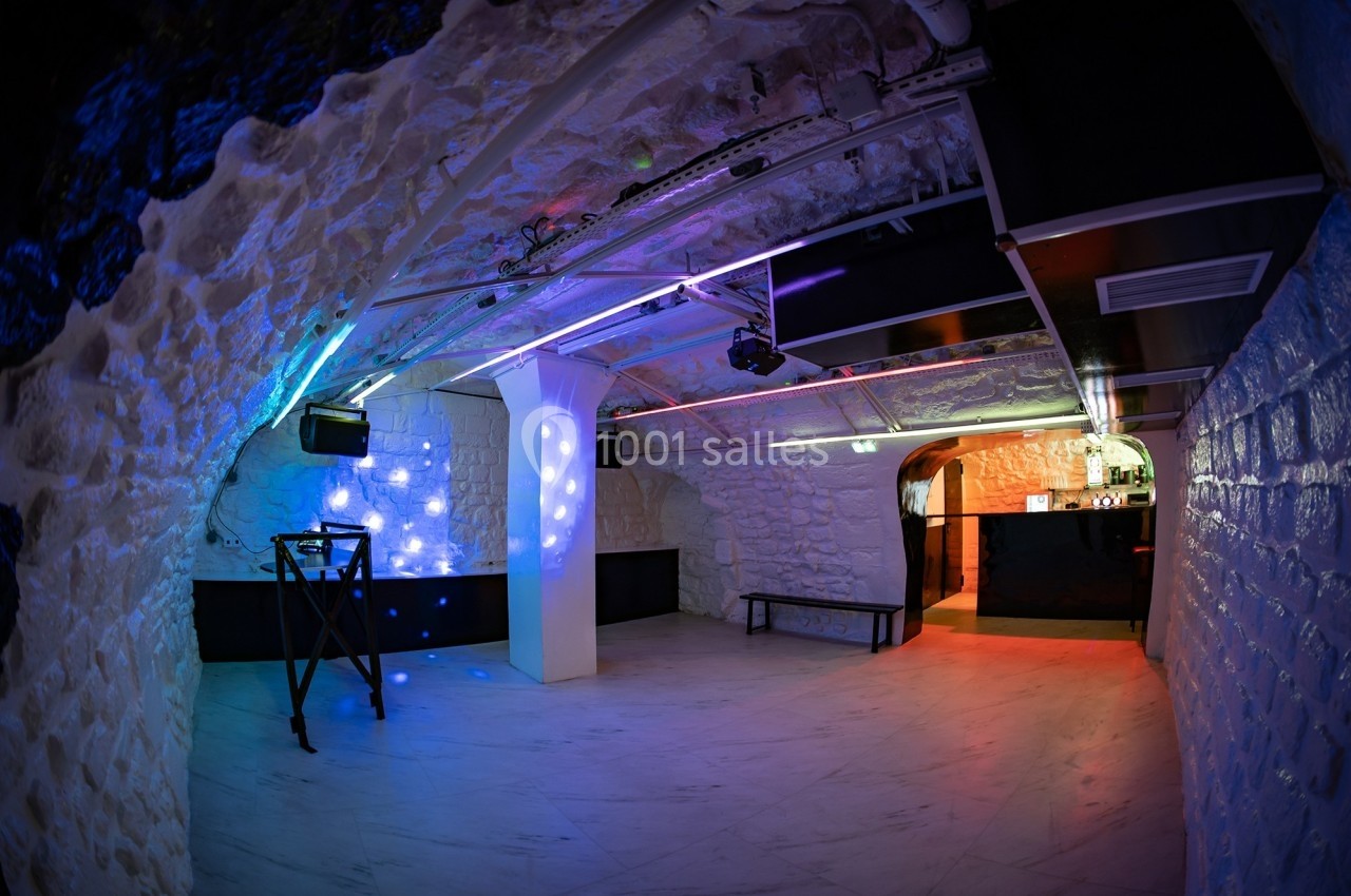 Salle voûtée avec murs en pierre, éclairage coloré, piste de danse et comptoir de bar en arrière-plan.