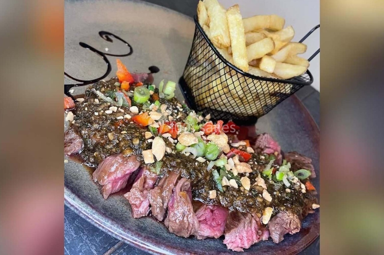Assiette de viande grillée garnie de sauce aux herbes, légumes et cacahuètes, accompagnée de frites dans un panier.