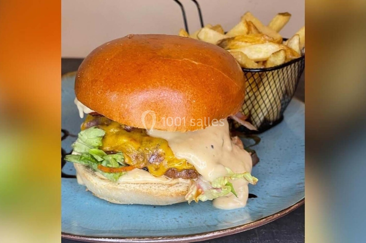 Burger garni de fromage fondu, salade et sauce, servi avec des frites dans une corbeille sur une assiette bleue.