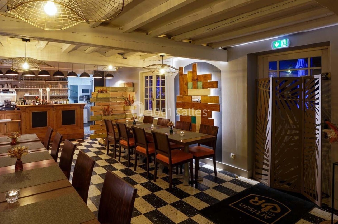 Salle de restaurant chaleureuse avec tables en bois, éclairage tamisé et vue sur un comptoir en arrière-plan.