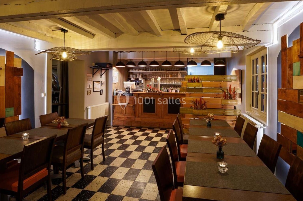 Salle de restaurant chaleureuse avec tables alignées, décor en bois et éclairage suspendu dans une ambiance cosy.