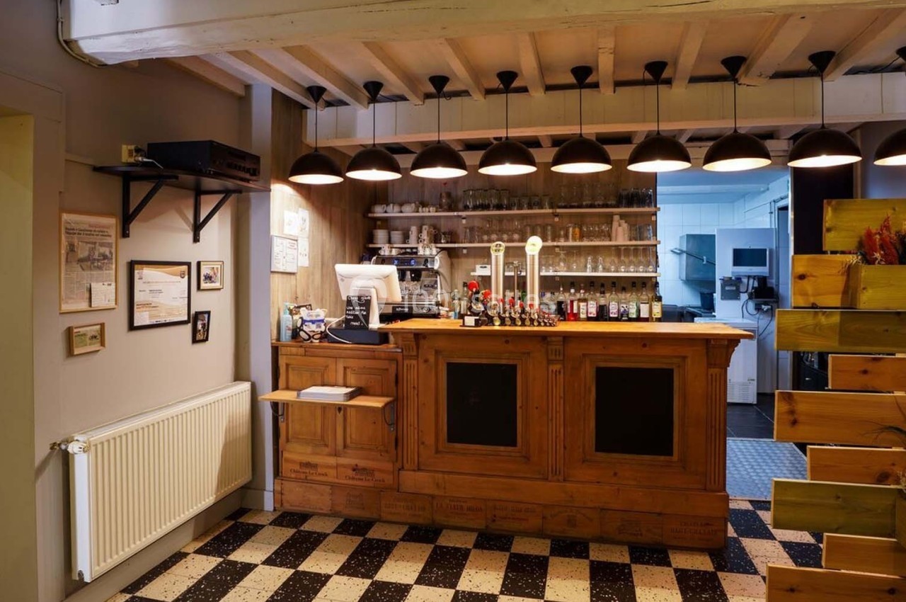 Comptoir en bois dans un bar avec éclairage suspendu, étagères de verres et décoration murale simple.