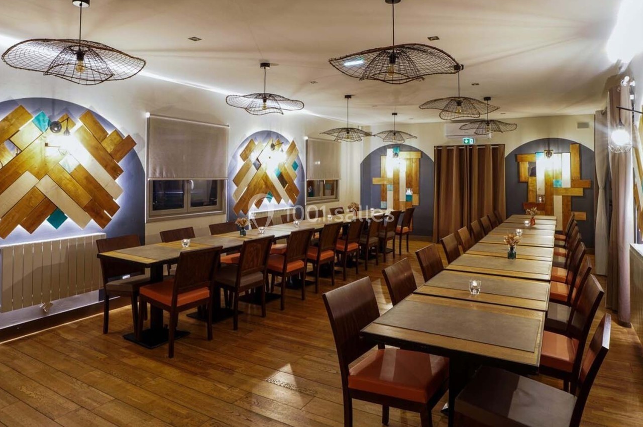 Salle de restaurant moderne avec longues tables en bois, chaises rembourrées et décorations murales géométriques.