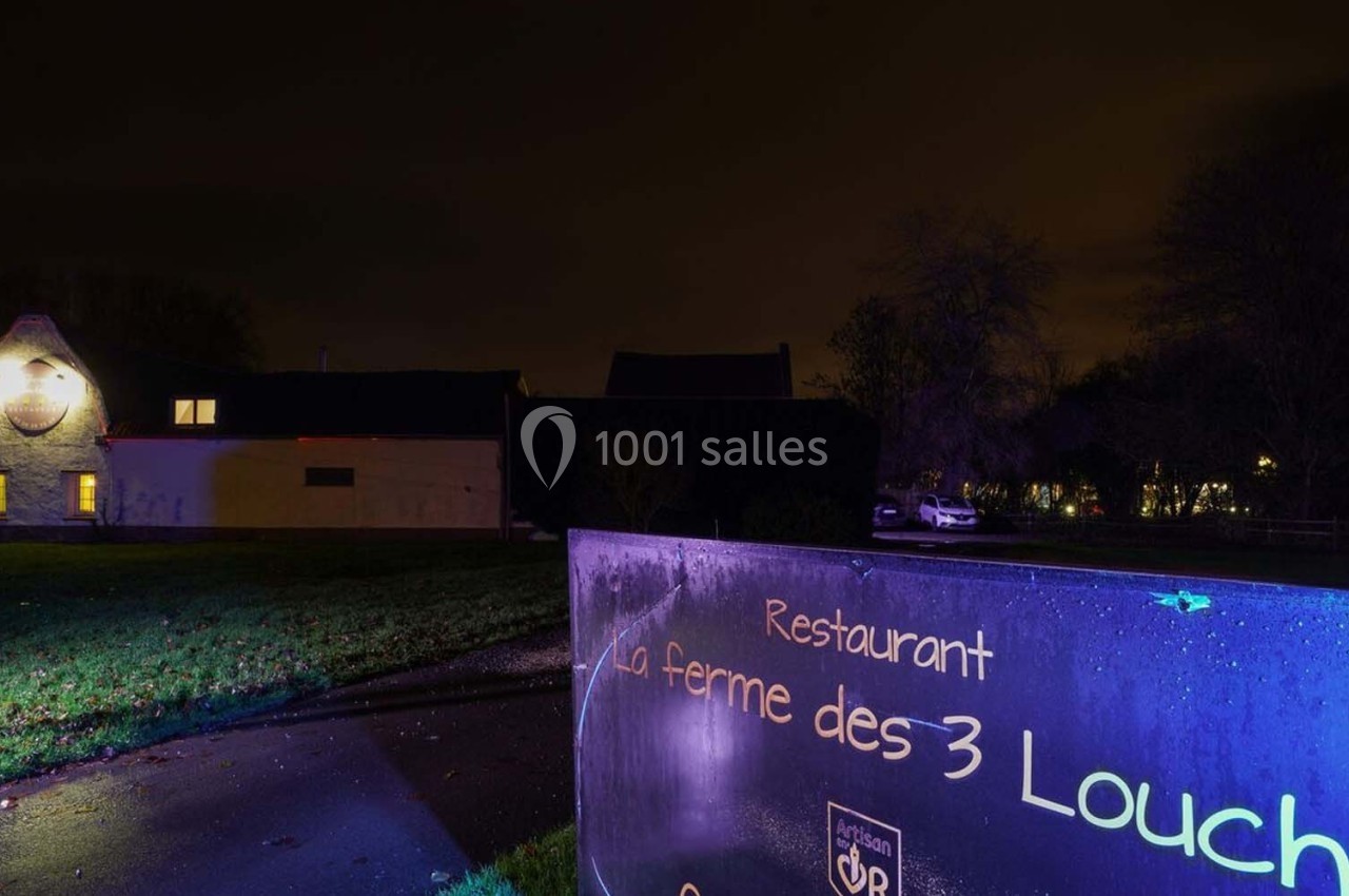 Vue nocturne d'un restaurant avec un panneau indiquant ’La ferme des 3 Louches’ et un bâtiment éclairé en arrière-plan.