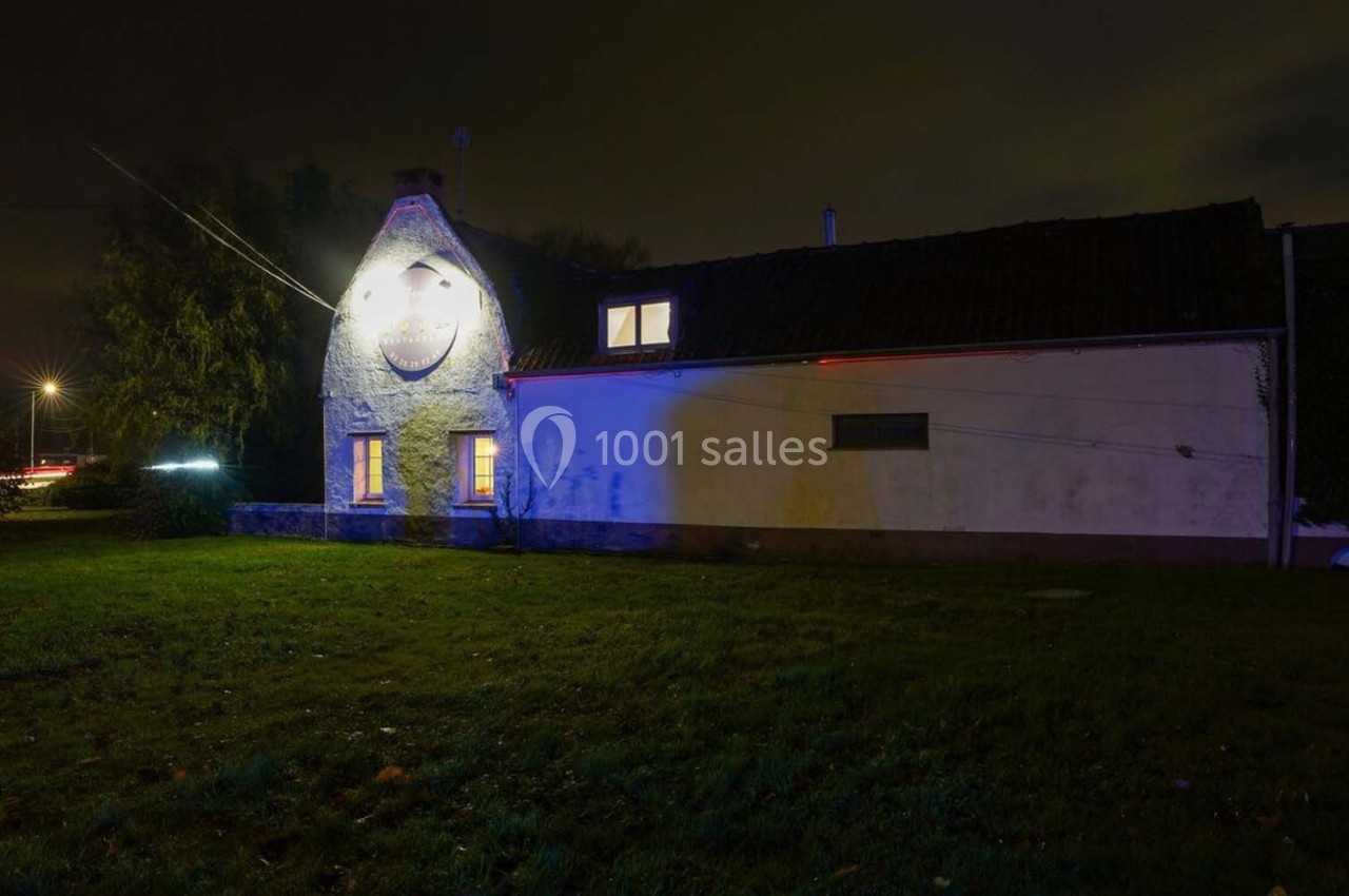 Façade d'une maison éclairée par des lumières colorées dans un environnement nocturne avec un jardin à l'avant.