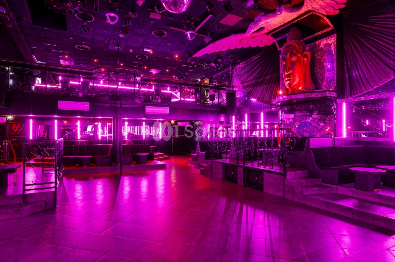 Salle de discothèque vide avec éclairage néon rose, décorations exotiques et sièges disposés autour de la piste.