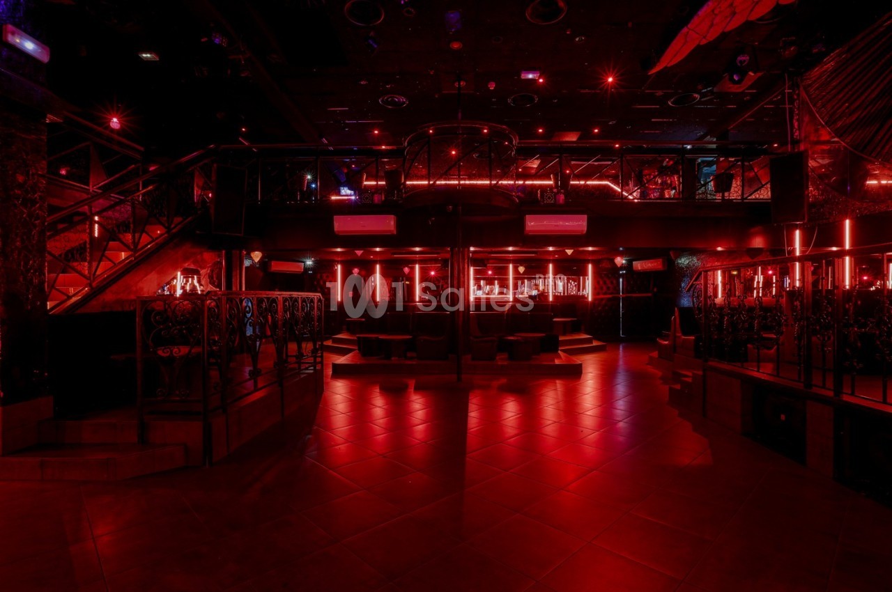 Intérieur d'une discothèque avec éclairage rouge, bar central, mezzanine et escaliers métalliques.